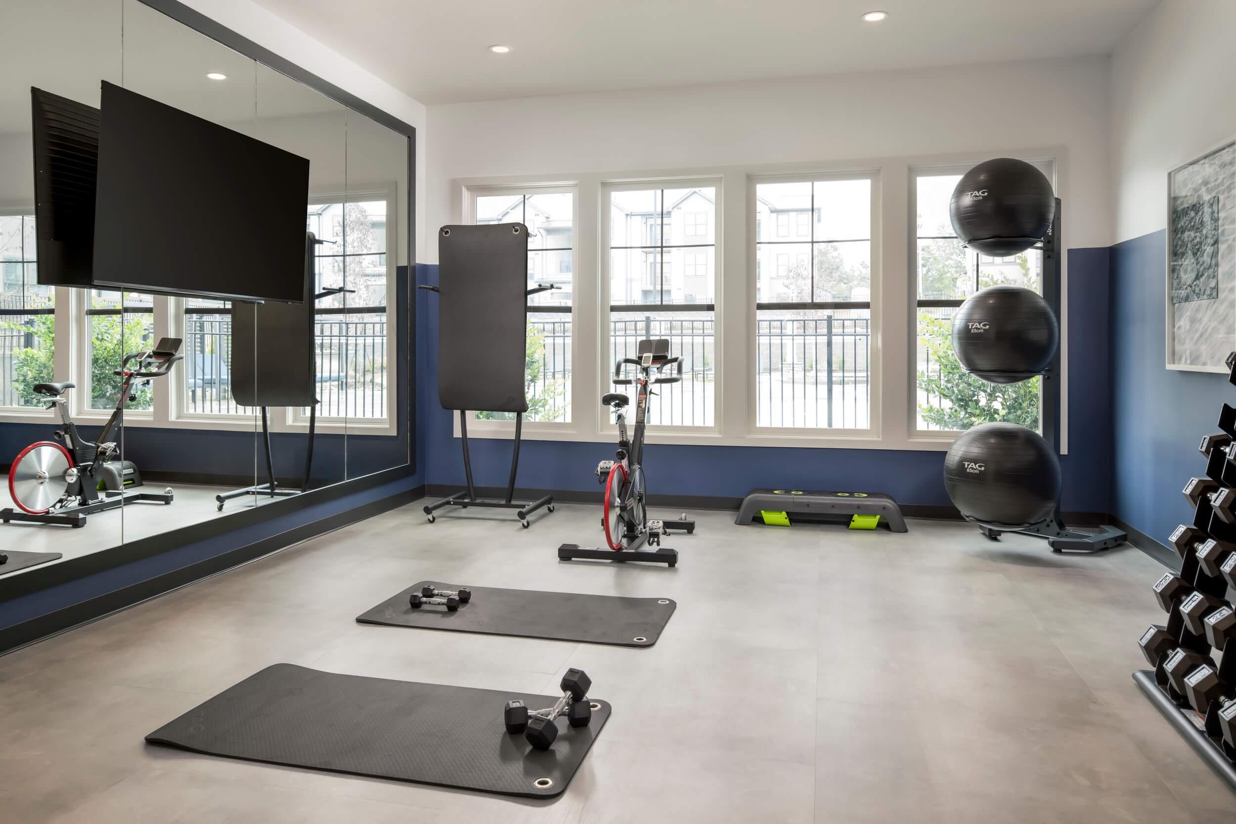 Evolve Deep River modern gym room with exercise mats, weights, stationary bike, balance balls, and large wall mirror.