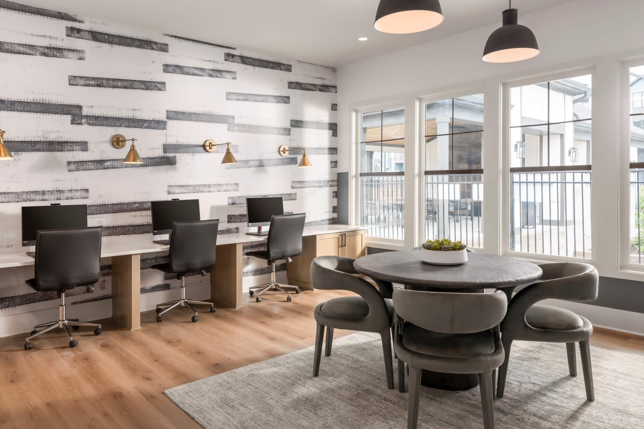 Evolve Deep River modern office space with four computer workstations and a round table with chairs near large windows.